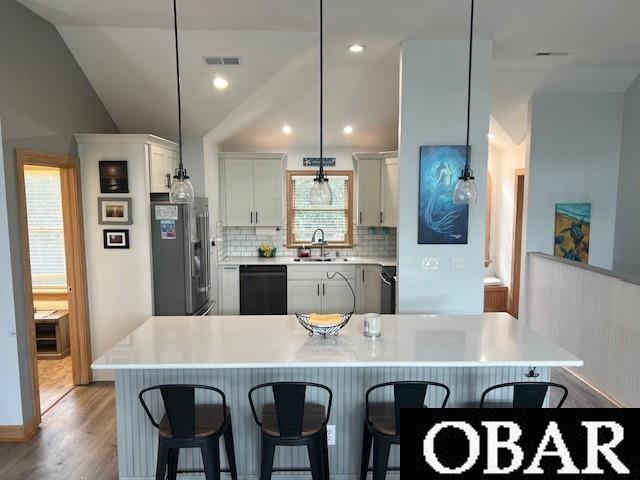 kitchen featuring visible vents, a kitchen bar, lofted ceiling, black dishwasher, and stainless steel fridge