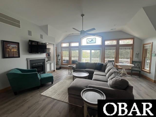 living area featuring a glass covered fireplace, lofted ceiling, light wood-style floors, and visible vents