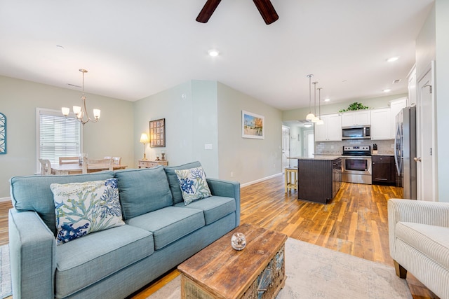 living room featuring recessed lighting, ceiling fan with notable chandelier, light wood-type flooring, and baseboards