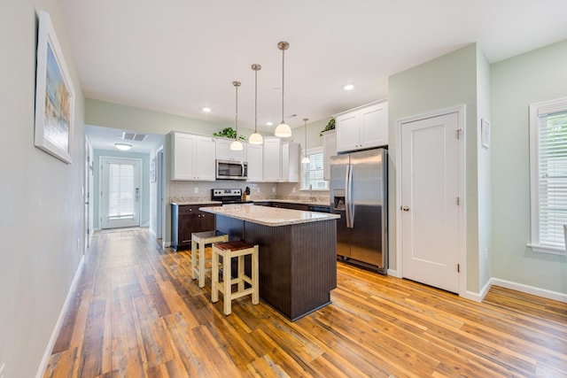 kitchen with tasteful backsplash, a center island, light wood-type flooring, appliances with stainless steel finishes, and white cabinets