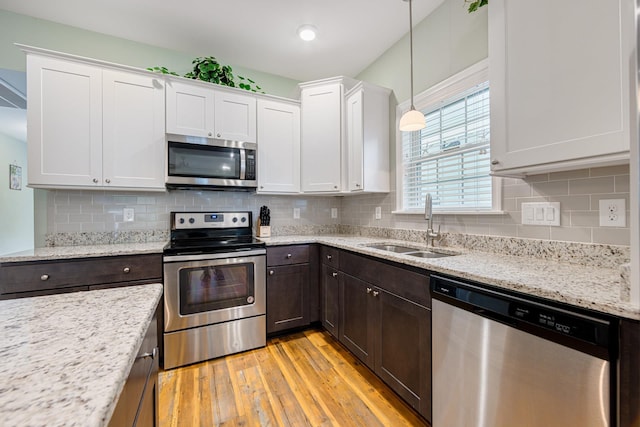 kitchen with a sink, stainless steel appliances, dark brown cabinetry, white cabinets, and light wood finished floors