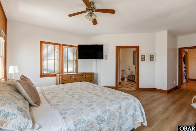 bedroom featuring stacked washer / drying machine, ceiling fan, ensuite bath, baseboards, and wood finished floors
