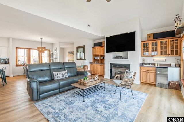 living area featuring light wood-style floors, baseboards, a fireplace, a ceiling fan, and wet bar