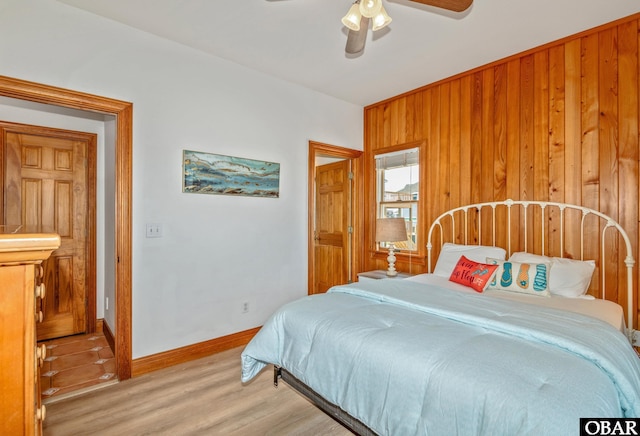 bedroom featuring wooden walls, light wood-type flooring, baseboards, and ceiling fan