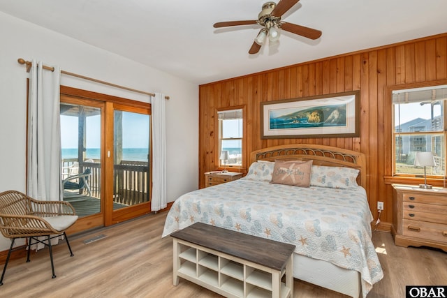 bedroom featuring light wood-type flooring, access to outside, wooden walls, and multiple windows