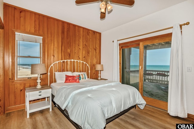 bedroom featuring access to exterior, ceiling fan, wooden walls, and wood finished floors