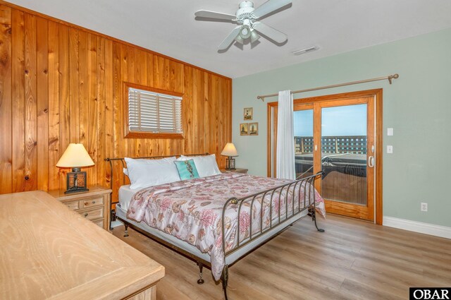 bedroom featuring visible vents, baseboards, wooden walls, light wood finished floors, and access to outside
