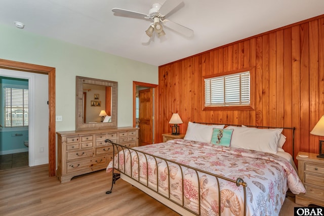 bedroom featuring wood walls, a ceiling fan, light wood finished floors, and baseboards