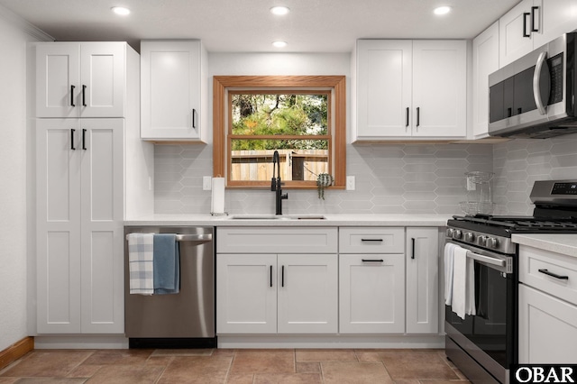 kitchen featuring stainless steel appliances, light countertops, white cabinetry, a sink, and recessed lighting