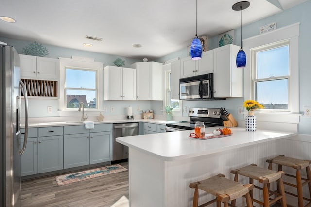 kitchen featuring a peninsula, gray cabinets, stainless steel appliances, light countertops, and a sink