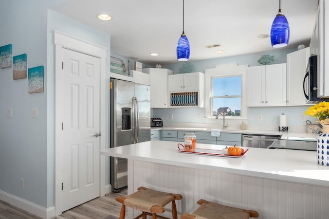 kitchen with light countertops, appliances with stainless steel finishes, white cabinets, and pendant lighting