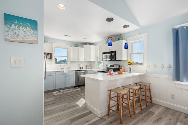 kitchen featuring appliances with stainless steel finishes, a peninsula, light countertops, a kitchen bar, and white cabinetry