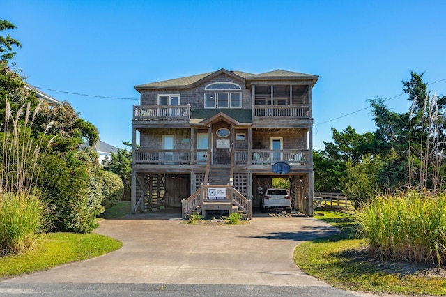 coastal inspired home featuring covered porch, a sunroom, concrete driveway, stairway, and a carport