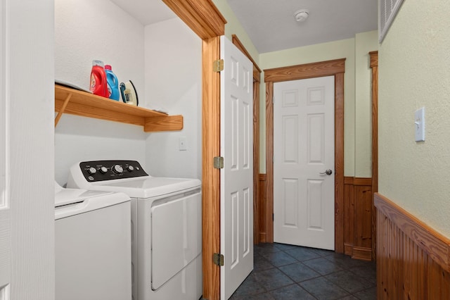 clothes washing area with washing machine and dryer, laundry area, a wainscoted wall, and dark tile patterned floors