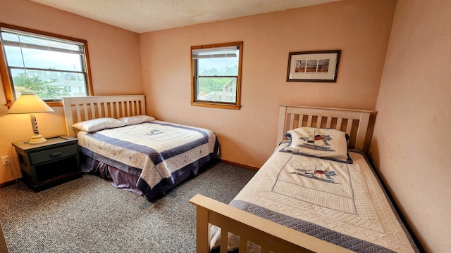 bedroom with multiple windows, dark carpet, and a textured ceiling