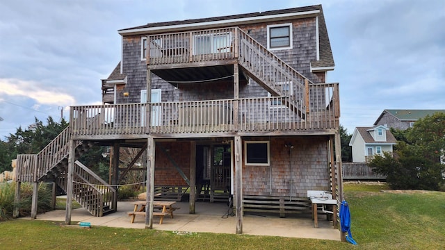 rear view of property featuring a shingled roof, a lawn, a patio, stairway, and a wooden deck