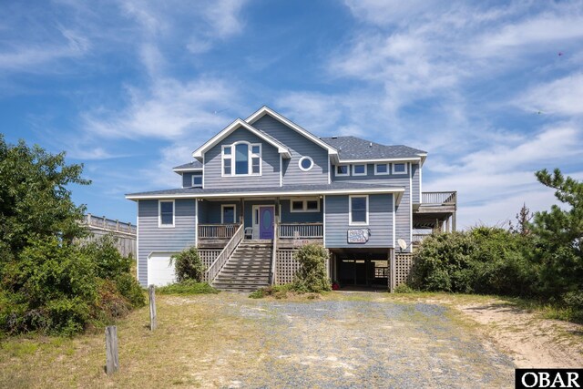 coastal inspired home featuring dirt driveway, a porch, an attached garage, and stairs