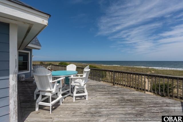 wooden deck featuring a view of the beach, a water view, and outdoor dining space