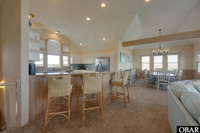 kitchen featuring light stone counters, pendant lighting, open floor plan, vaulted ceiling, and stainless steel fridge with ice dispenser