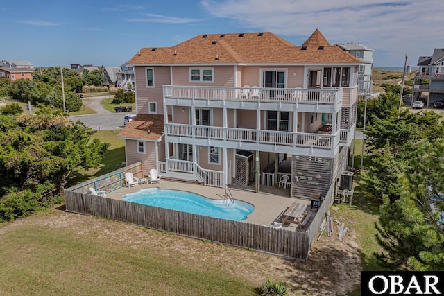 rear view of house with a fenced in pool, a fenced backyard, a yard, and a balcony