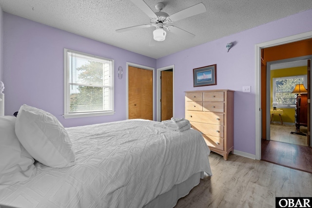 bedroom with light wood-type flooring, ceiling fan, baseboards, and a textured ceiling