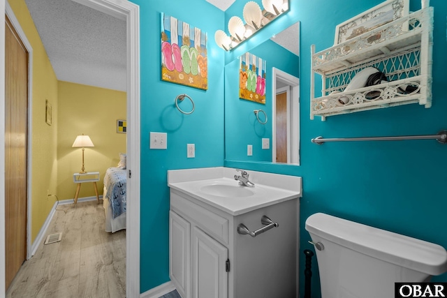 half bathroom with baseboards, toilet, wood finished floors, a textured ceiling, and vanity