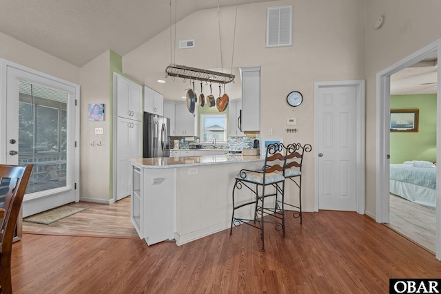 kitchen with light wood finished floors, visible vents, white cabinetry, a peninsula, and stainless steel refrigerator