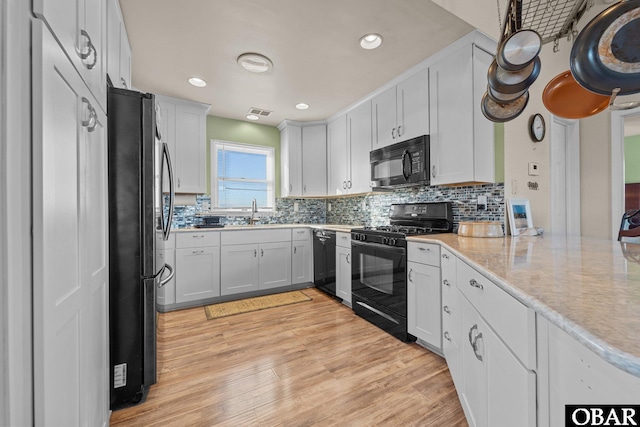 kitchen with light wood finished floors, recessed lighting, decorative backsplash, white cabinetry, and black appliances