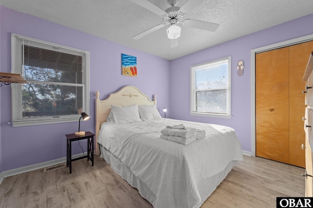 bedroom featuring light wood-type flooring, visible vents, a textured ceiling, and baseboards