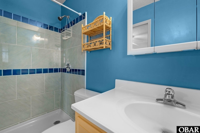 full bathroom featuring tiled shower, vanity, and toilet