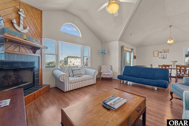 living area with a textured ceiling, wood finished floors, a ceiling fan, vaulted ceiling, and a tiled fireplace