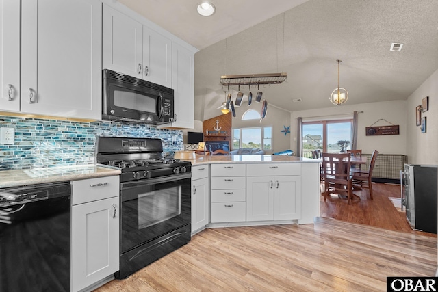 kitchen featuring lofted ceiling, black appliances, white cabinetry, and decorative light fixtures