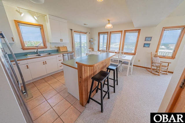 kitchen featuring white cabinets, stainless steel dishwasher, a sink, and a breakfast bar area
