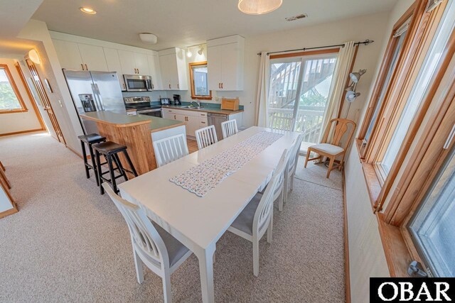 dining space with a healthy amount of sunlight, light colored carpet, and visible vents