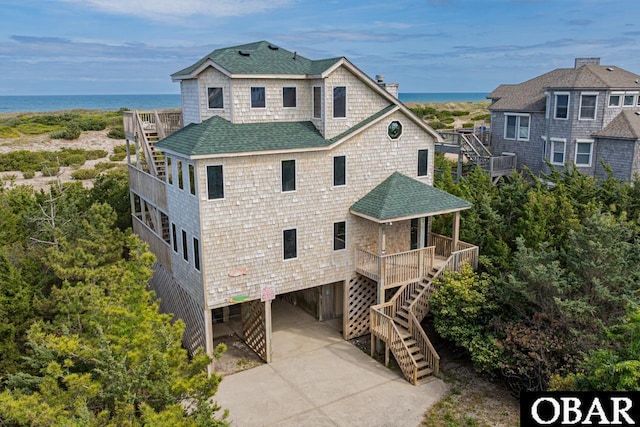 exterior space featuring a chimney, a carport, a water view, a shingled roof, and stairs