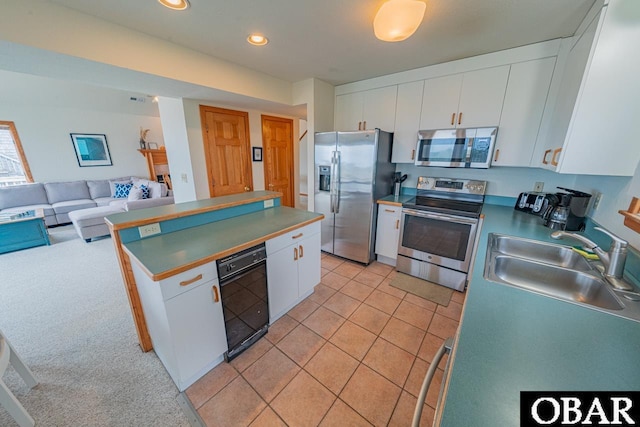 kitchen with a sink, open floor plan, white cabinets, appliances with stainless steel finishes, and recessed lighting