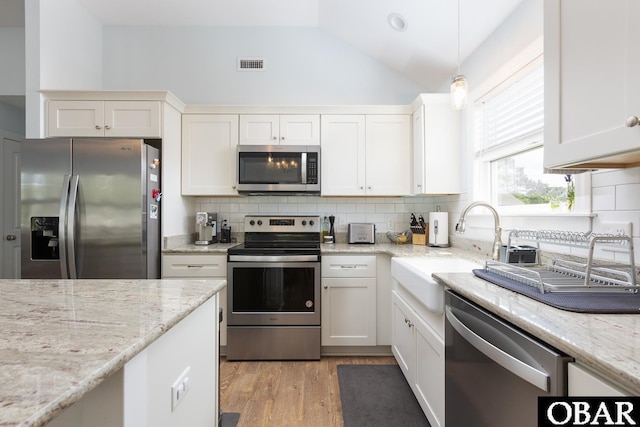 kitchen featuring stainless steel appliances, a sink, vaulted ceiling, backsplash, and light wood-style flooring