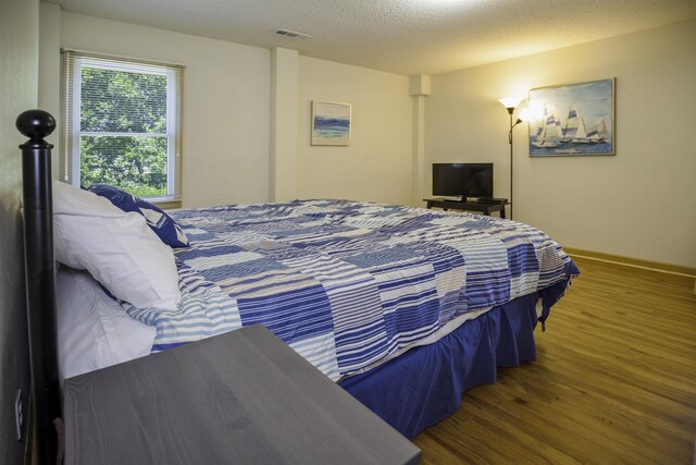 bedroom featuring visible vents, a textured ceiling, baseboards, and wood finished floors