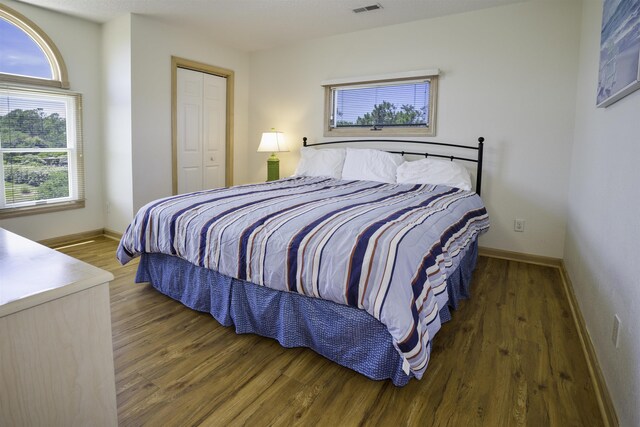 bedroom with a closet, dark wood finished floors, visible vents, and baseboards