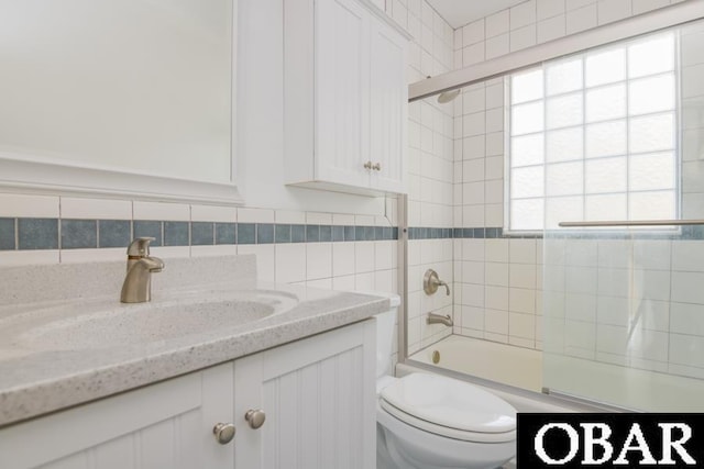 full bath featuring combined bath / shower with glass door, tile walls, toilet, and vanity