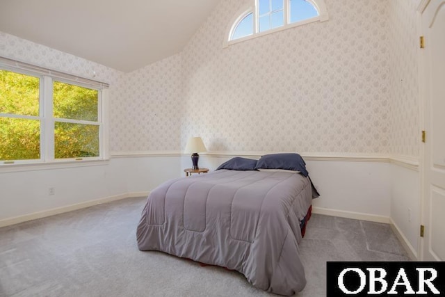 bedroom featuring lofted ceiling, light colored carpet, a wainscoted wall, baseboards, and wallpapered walls