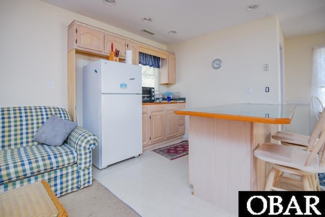 kitchen with a breakfast bar area, recessed lighting, visible vents, freestanding refrigerator, and light brown cabinets