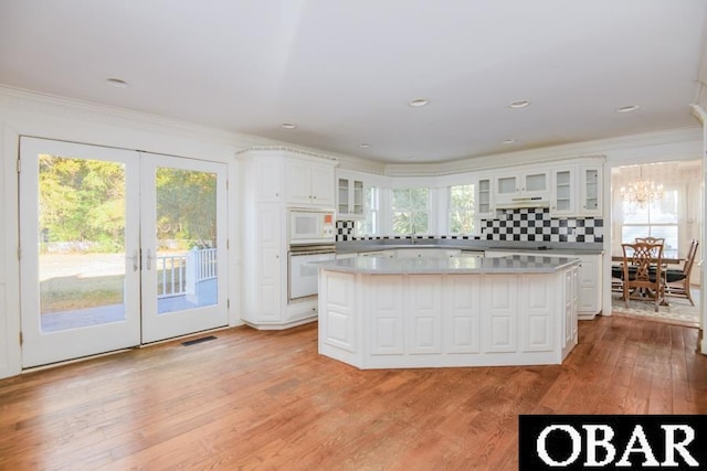 kitchen with white appliances, a kitchen island, white cabinets, light countertops, and glass insert cabinets