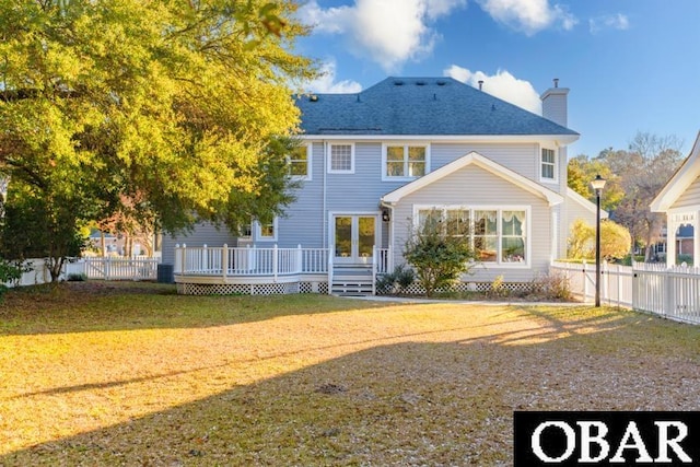 back of property with a fenced backyard, a chimney, roof with shingles, a deck, and a yard