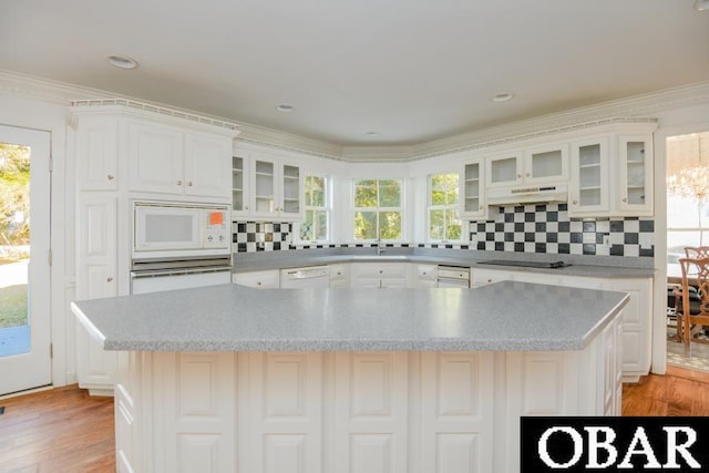 kitchen with under cabinet range hood, white appliances, white cabinets, a large island, and glass insert cabinets