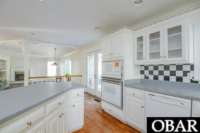 kitchen featuring white appliances, white cabinetry, glass insert cabinets, and light countertops