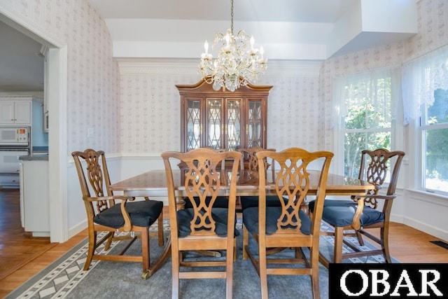 dining space featuring wallpapered walls, a notable chandelier, baseboards, and wood finished floors