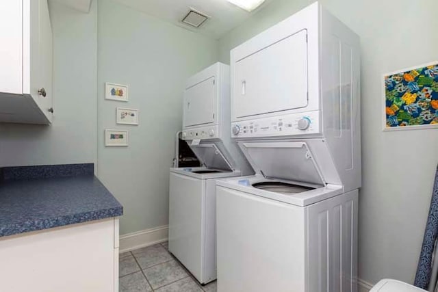 laundry area with visible vents, stacked washing maching and dryer, cabinet space, light tile patterned flooring, and baseboards