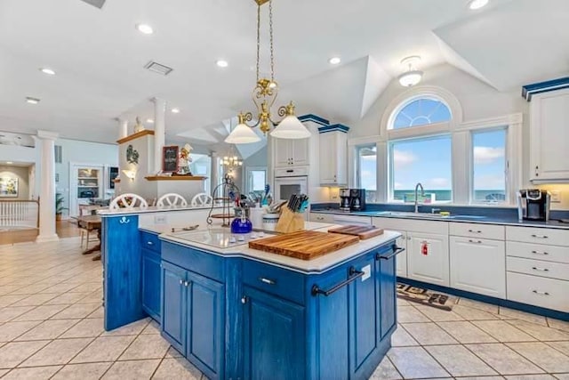 kitchen featuring a notable chandelier, blue cabinetry, white appliances, light tile patterned floors, and decorative columns