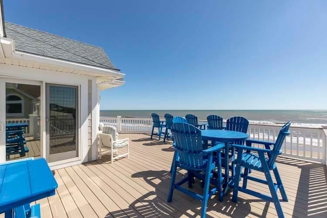 wooden deck with outdoor dining space, a view of the beach, and a water view